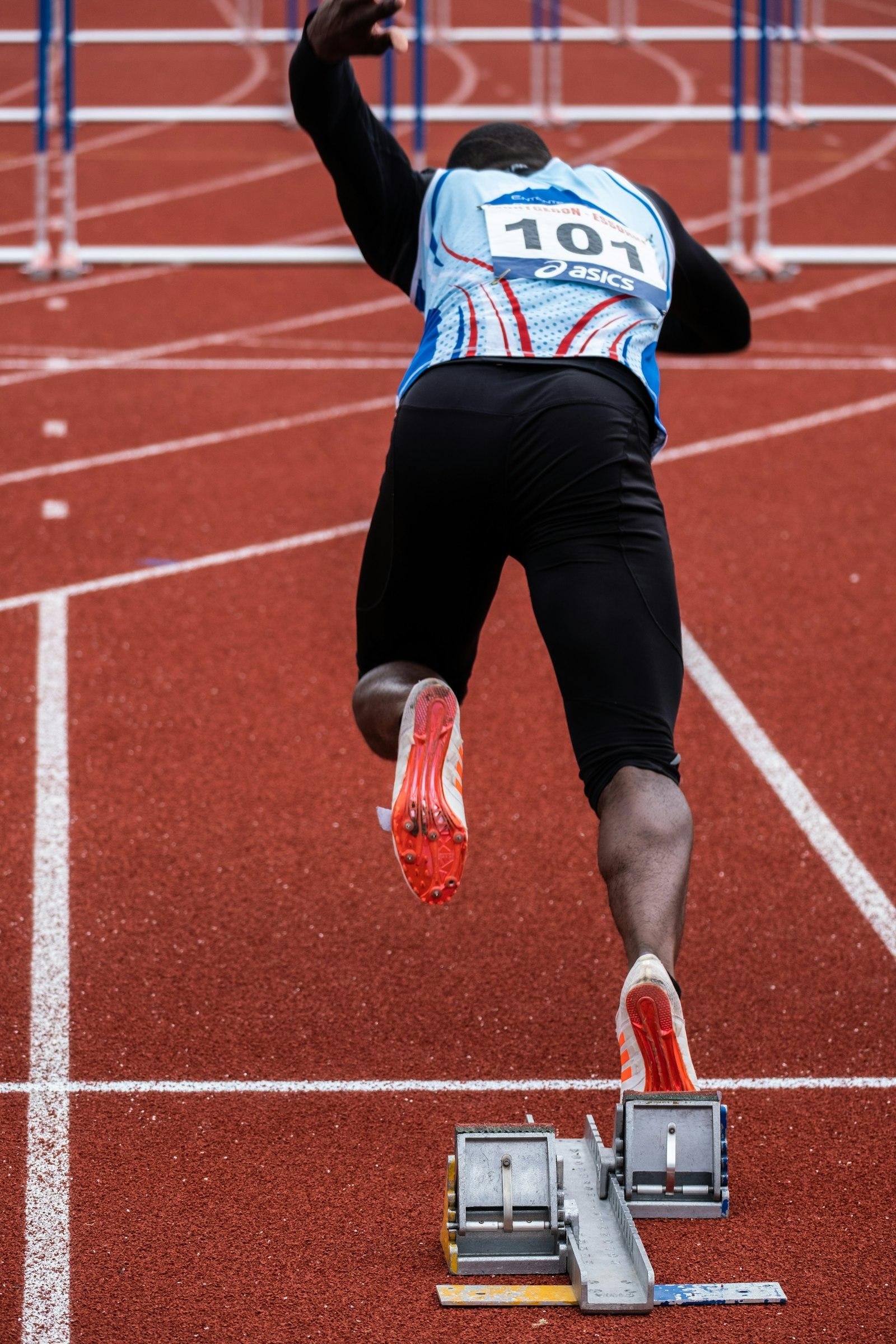 Sprinter exploding out of the starting blocks on a red athletics track