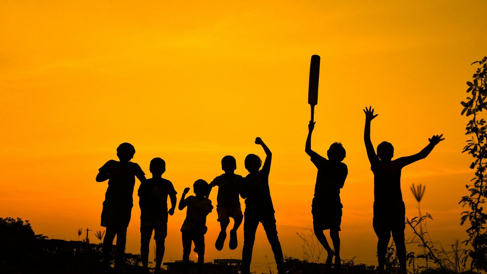 Silhouettes of children celebrating on a field at sunset